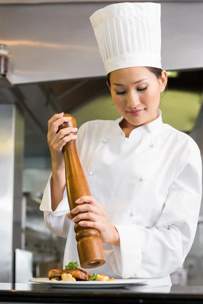 Female cook grinding pepper on food in kitchen — Stock Photo, Image