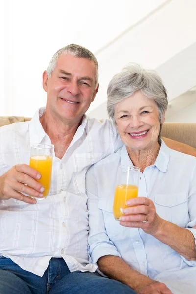 Äldre par sitter på soffan dricka apelsinjuice — Stockfoto