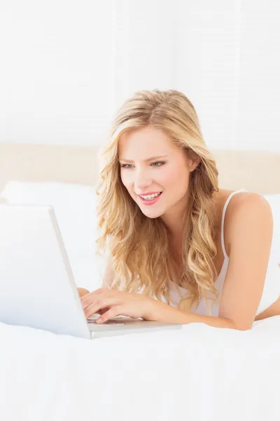 Blonde lying on her bed using laptop — Stock Photo, Image