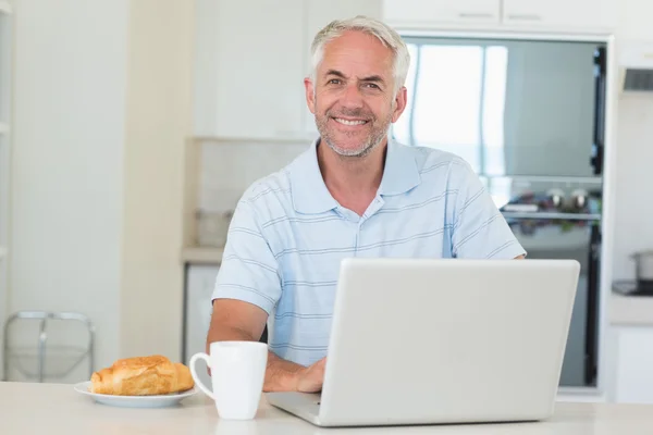快乐的人在吃早饭时使用他的笔记本电脑 — 图库照片
