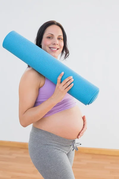 怀孕的妇女抱着运动垫着相机微笑 — 图库照片