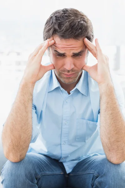 Wincing man with headache sitting on the couch — Stock Photo, Image