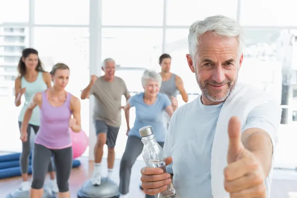 Senior gestikuliert mit Menschen, die im Fitnessstudio trainieren — Stockfoto