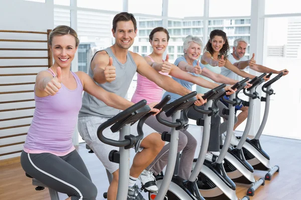 Gente haciendo ejercicio en la clase de spinning mientras hace gestos con los pulgares hacia arriba —  Fotos de Stock