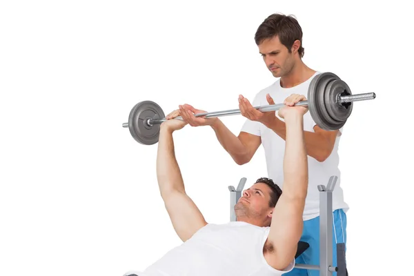 Trainer helping fit man to lift the barbell bench press — Stock Photo, Image