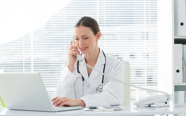 Médico usando teléfono fijo y portátil — Foto de Stock