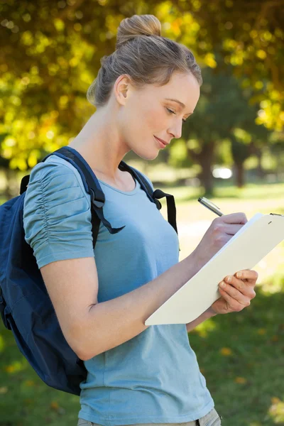 Beautiful young woman writing on clipboard at park — Stock Photo, Image