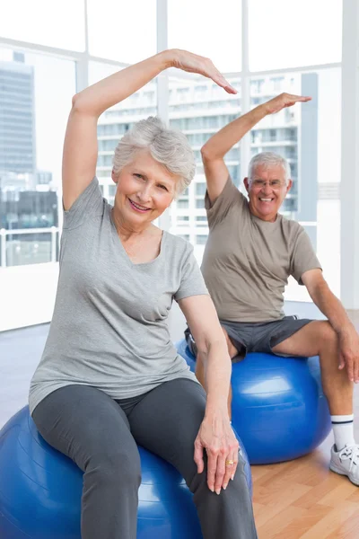 Старшая пара делает упражнения на растяжку на фитнес-мячи — стоковое фото