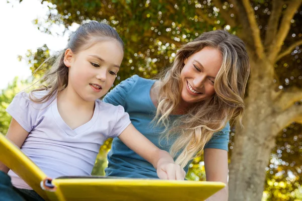 Glückliche Mutter und Tochter lesen im Park ein Buch — Stockfoto