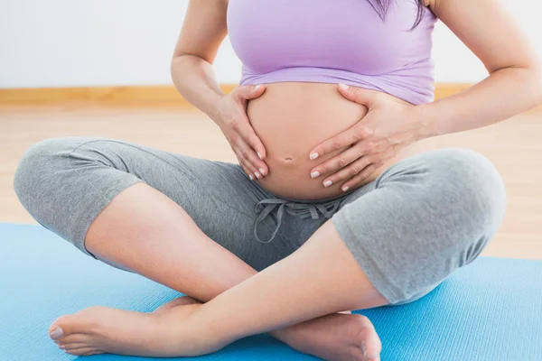 Pregnant woman sitting on mat in touching her belly — Stock Photo, Image