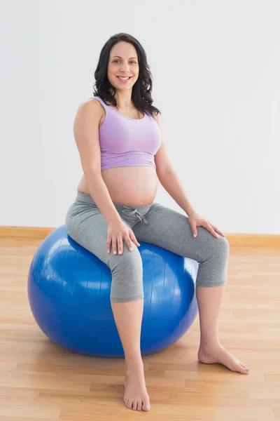 Mujer embarazada sentada en bola de ejercicio azul sonriendo a la cámara — Foto de Stock