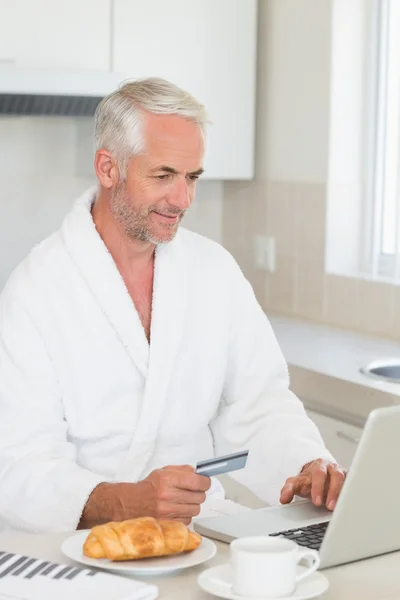 Gelukkig man online winkelen bij het ontbijt in een badjas — Stockfoto