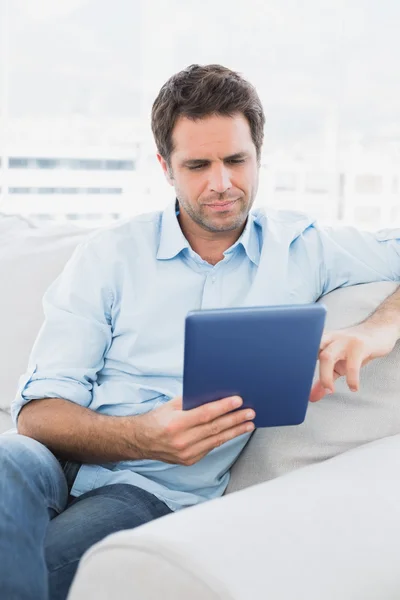 Hombre guapo sentado en el sofá utilizando su PC tableta —  Fotos de Stock