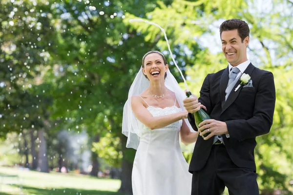 Pareja recién casada haciendo estallar corcho de champán — Foto de Stock
