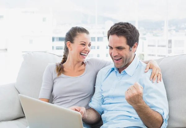 Casal animado sentado no sofá usando laptop juntos — Fotografia de Stock
