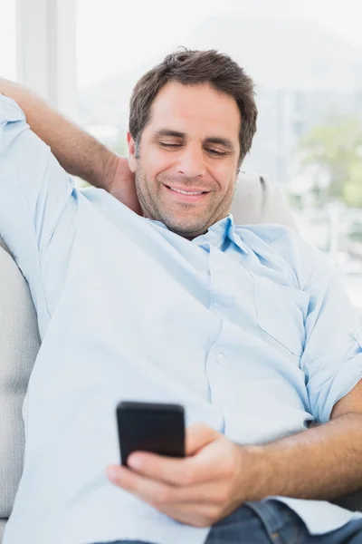 Uomo sorridente seduto sul divano che messaggia sul suo telefono — Foto Stock