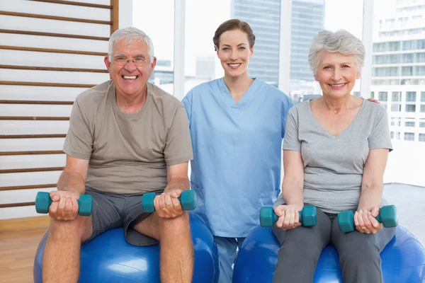 Female therapist assisting senior couple with dumbbells — Stock Photo, Image