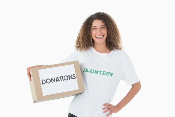 Voluntario sonriente sosteniendo una caja de donaciones con la mano en la cadera — Foto de Stock