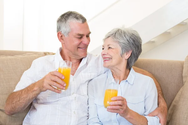 Starszy para siedzi kanapie, picie soku pomarańczowego — Zdjęcie stockowe