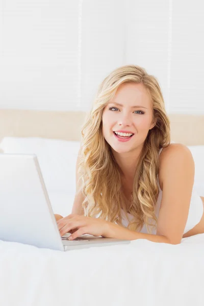 Blonde lying on her bed using laptop — Stock Photo, Image