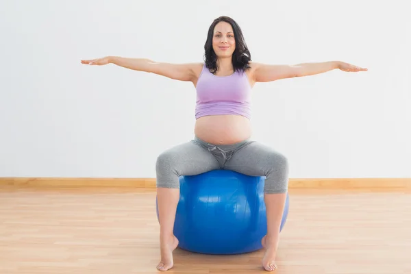 Беременная женщина сидит на синем шаре с вытянутыми руками — стоковое фото