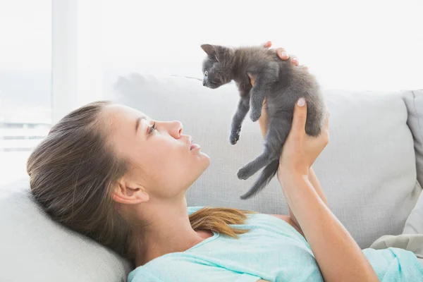 Весела жінка лежить на дивані тримає сірого кошеня — стокове фото