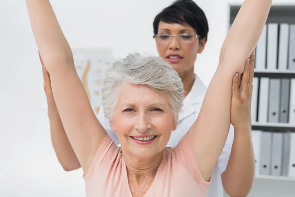 Fisioterapeuta femenina con mujer mayor levantando las manos — Foto de Stock