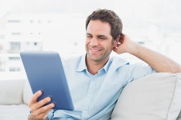 Beau homme assis sur le canapé en utilisant sa tablette — Photo