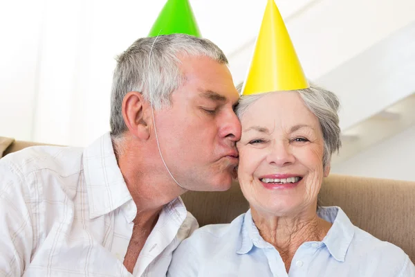 Coppia anziana seduta sul divano indossando cappelli da festa — Foto Stock
