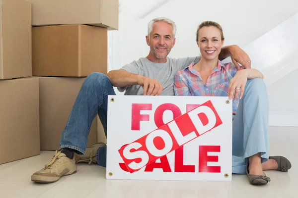 Pareja feliz sentada en el suelo con letrero vendido — Foto de Stock