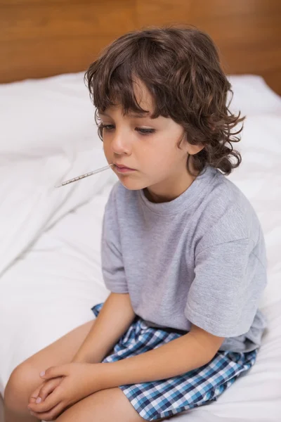 Chore dziecko z termometrem, siedząc na łóżku — Zdjęcie stockowe