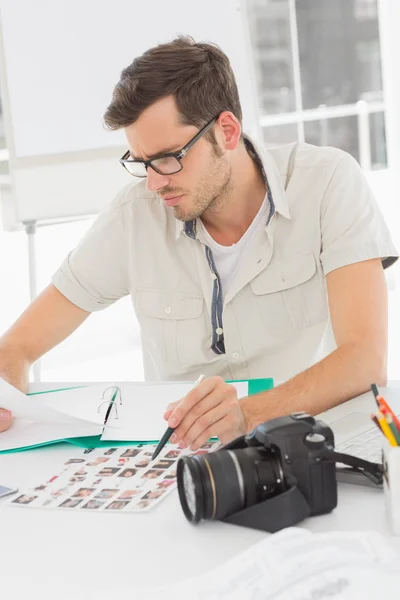 Artista masculino concentrado sentado en el escritorio con fotos —  Fotos de Stock