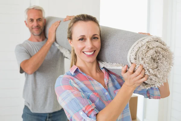 Happy couple carrying a rolled up rug together — Stock Photo, Image