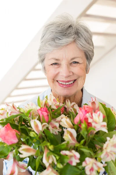 Retired woman holding bouquet of flowers smiling at camera — Stock Photo, Image