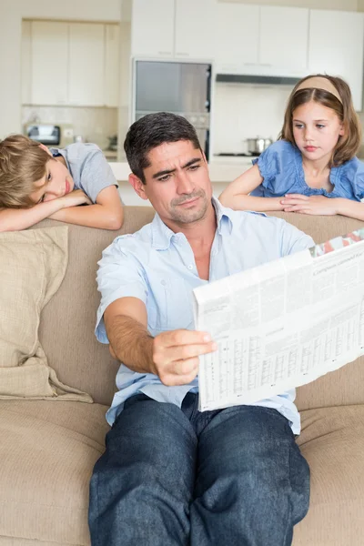 Dzieci patrząc na ojca czytanie gazety — Zdjęcie stockowe