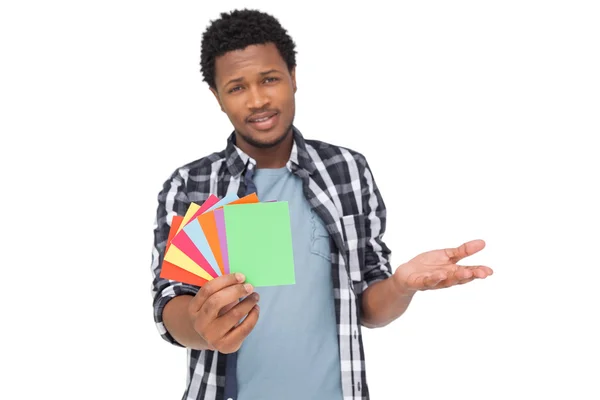 Retrato de un hombre confundido sosteniendo papeles de colores — Foto de Stock