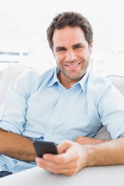 Fröhlicher Mann, der auf der Couch sitzt und einen Text schickt — Stockfoto