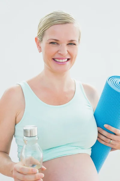 Беременная женщина с бутылкой воды и ковриком для упражнений улыбается — стоковое фото