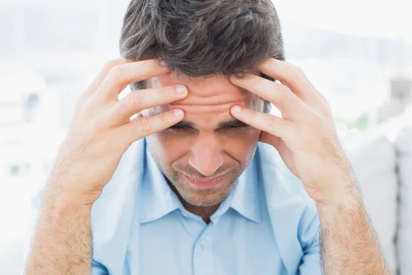 Attraktiver Mann sitzt mit Kopfschmerzen auf der Couch — Stockfoto