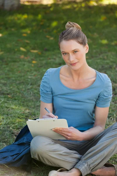 Mujer joven relajada escribiendo en el portapapeles en el parque — Foto de Stock