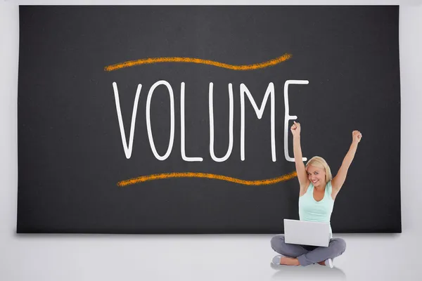 Juichende blonde met behulp van laptop tegen het woord volume — Stockfoto