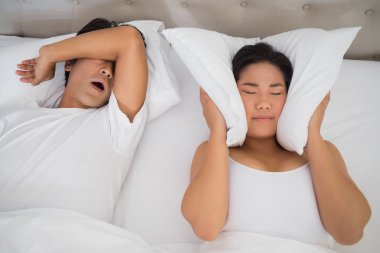 Annoyed woman covering her ears with pillows to block out snoring clipart
