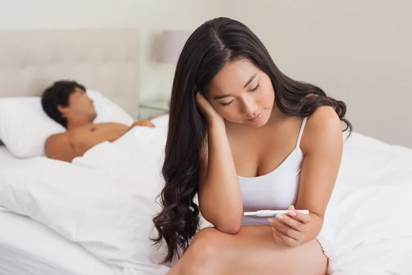 Frau sitzt auf Bett und hält Schwangerschaftstest, während Freund schläft — Stockfoto