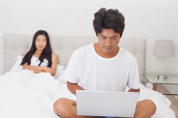 Mujer viendo novio usando el ordenador portátil en el extremo de la cama — Foto de Stock