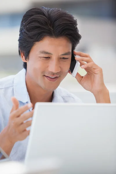Šťastný muž pomocí jeho laptop mluví po telefonu — Stockfoto