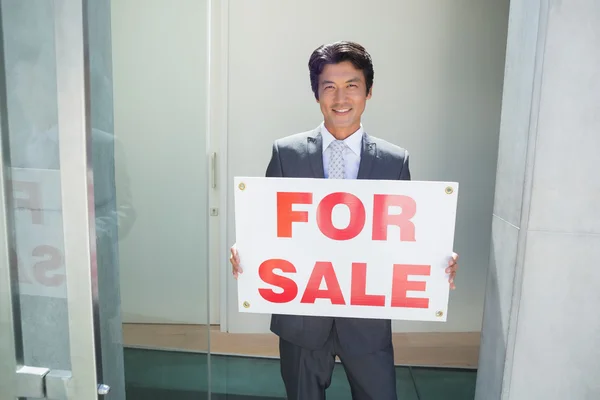 Agent immobilier confiant debout à la porte d'entrée montrant à vendre signe — Photo
