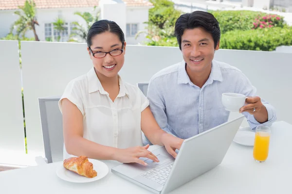 Sorrindo casal tomando café da manhã juntos usando laptop — Fotografia de Stock