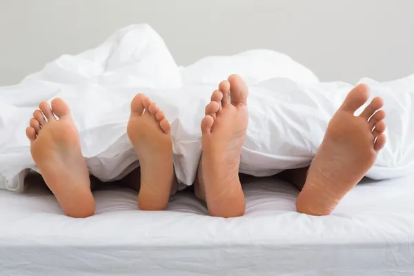 Couples feet sticking out from under duvet — Stock Photo, Image