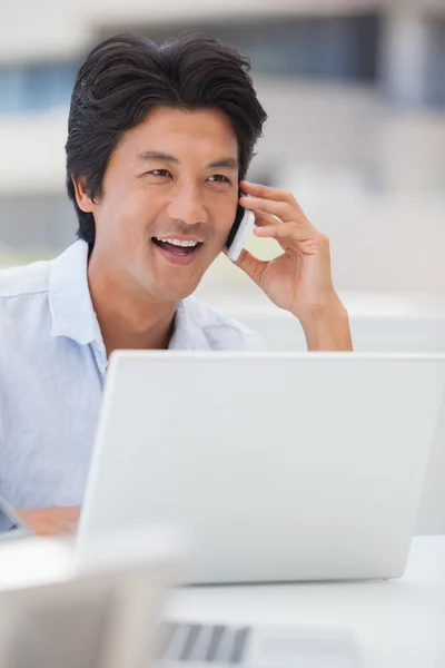 Šťastný muž pomocí jeho laptop mluví po telefonu — Stockfoto