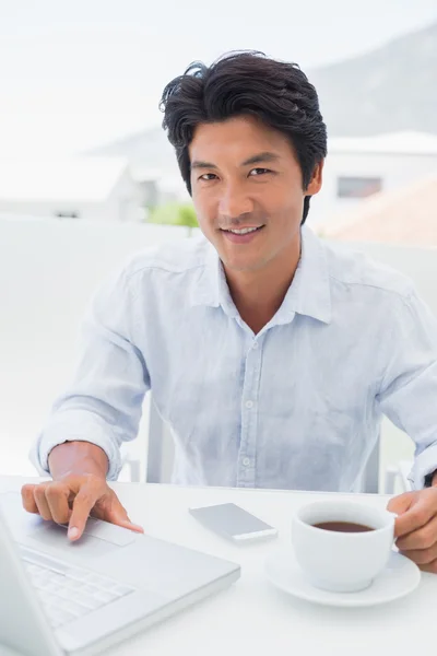 Hombre sonriente tomando café y usando laptop —  Fotos de Stock